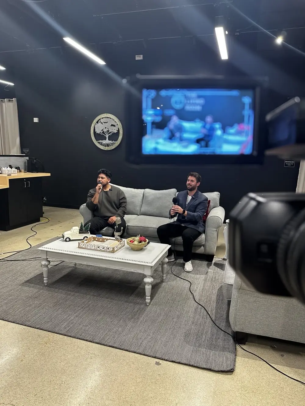 Dennis Hering and co-host Danny Ayala holding microphones on a studio couch during a live podcast recording